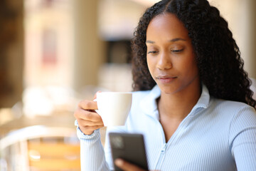 Black woman drinking coffee checking phone
