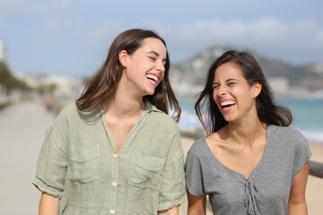 Two joyful friends walking and laughing on the beach