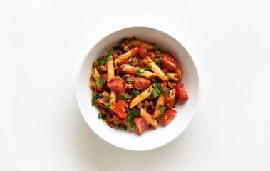 Bowl of bolognese penne pasta with minced meat, tomatoes and greens