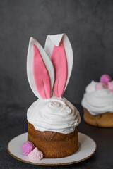 Beautiful stylish still life. Easter cake with rabbit ears, meringue, marshmallows, Easter eggs and willow twigs on a dark background. happy Easter 2024.
