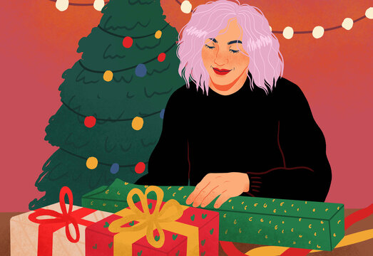 Woman wrapping Christmas gifts by Christmas tree with string lights

