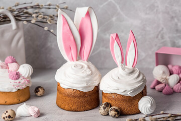 Beautiful stylish still life. Easter cake with rabbit (hare) ears, meringue, marshmallows, Easter eggs and willow branches and on a light concrete background. Happy Easter 2024.