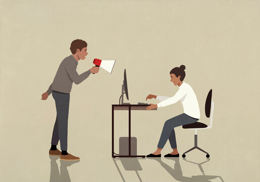 Businessman with bullhorn yelling at businesswoman working at computer in office
