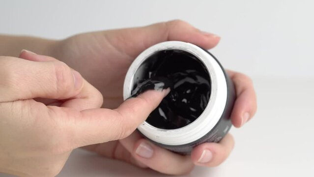 Woman finger touching black jelly mask for face, close up. A woman takes a black cream mask from a jar with her finger. The concept of skin care for the body and face. Macro.