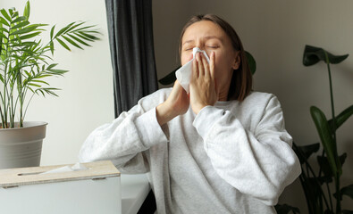 Sick unhealthy woman sneezes in paper tissue for cold, sinusitis, allergies or winter virus at...