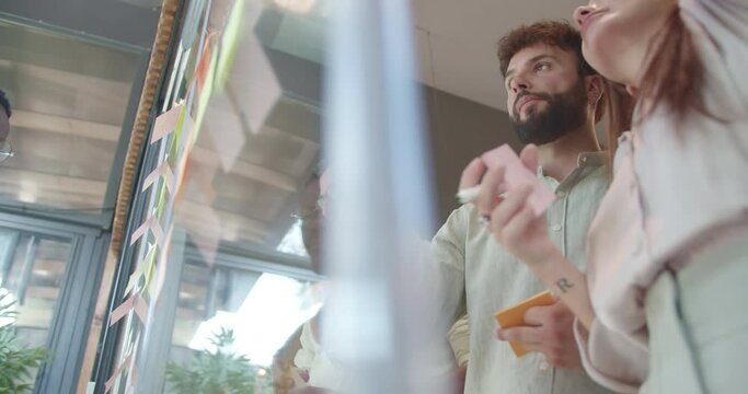 Happy, successful, diverse business team enjoying the music and dancing while writing business ideas on sticky notes over the glass wall. Businesspeople writing on sticky notes over a glass wall.