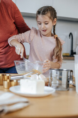 An 8-year-old Caucasian girl beats eggs with a whisk in a light kitchen.