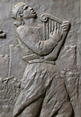 Bronze relief of a young man playing ancient harp while walking - 706366369