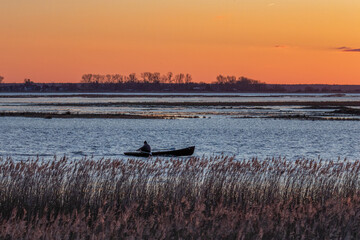 Naklejka premium Fischer mit Ruderboot bei Sonnenuntergang auf dem Bodden vor Zingst.