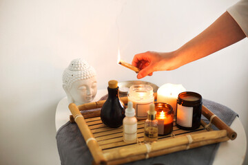 Female hand holding burning incense over wicker bamboo tray with candles and various oils in SPA