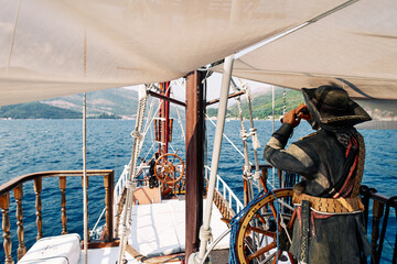Figure of a pirate with a telescope stands at the helm of a sailboat sailing on the sea. Back view