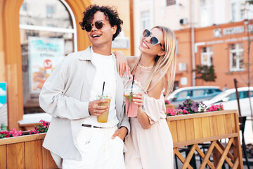 Young smiling beautiful woman and her handsome boyfriend in casual summer clothes. Happy cheerful family. Female having fun. Couple posing in street. Holding and drinking cocktail drink in plastic cup