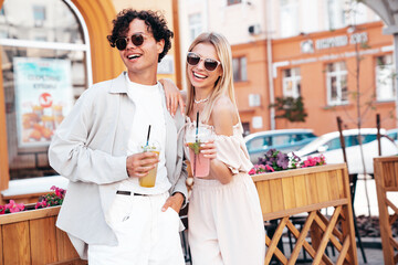 Young smiling beautiful woman and her handsome boyfriend in casual summer clothes. Happy cheerful family. Female having fun. Couple posing in street. Holding and drinking cocktail drink in plastic cup