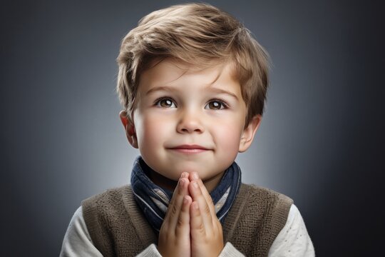 Adorable Young Boy with Hands Together on Gray Background