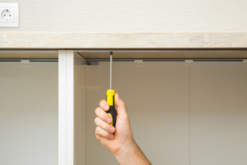 Young adult man hand using manual screwdriver and screwing screw in metal base cabinet frame and...