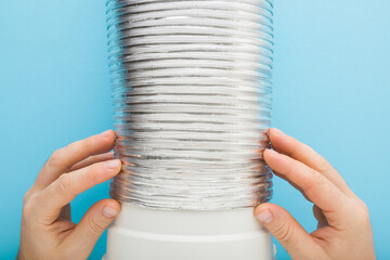 Man hands connecting corrugated aluminium pipe on plastic adapter on light blue background. Point...