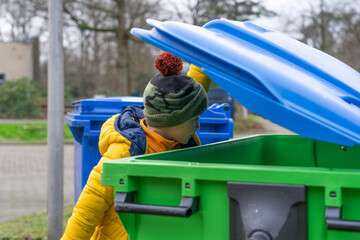 Boy throwing something into a garbage container and looking inside