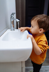 A little boy, full of wonder and curiosity, stands enchanted before a magical sink.