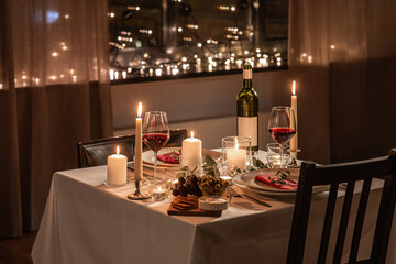 holidays, romantic date and celebration concept - close up of festive table serving for two with red wine in glasses, snacks and candles burning at home on valentine's day