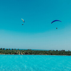 Two paragliders fly against the blue sky and azure water in the pool.