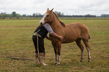 Naklejka na ściany i meble gaucho hugging his horse in the middle of the field