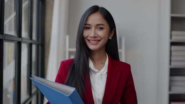 Businesswoman in red suit is standing and hold document paperwork folder working in the office with confident.