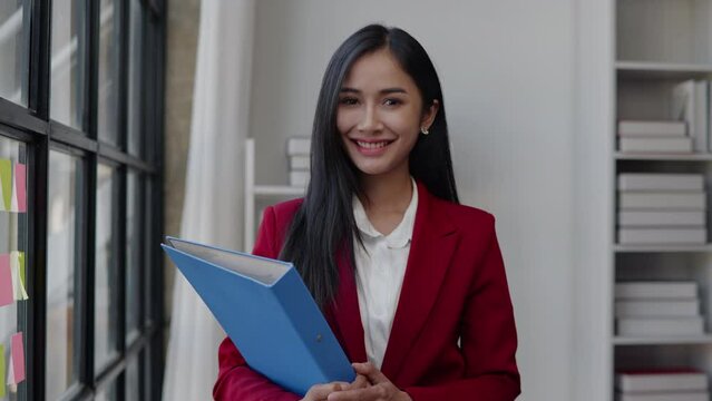 Businesswoman in red suit is standing and hold document paperwork folder working in the office with confident.
