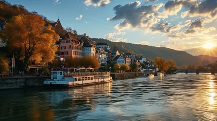 Fototapeten The setting sun illuminates the historic cityscape with a steamboat pier against the backdrop of a calm river and picturesque mountains © Kostya