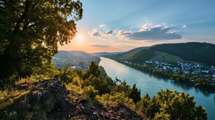 The setting sun shines over a winding river surrounded by wooded hills and vineyards, creating a picturesque landscape.