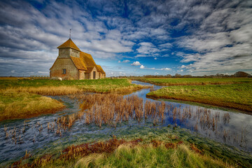 St Thomas Becket Church on the marshes  in the village of Fairfield on Romney Marsh in Kent surrounded by grazing sheep and water courses.