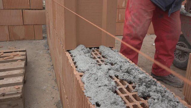 Detail of worker hands applying the mortar and placing a new brick on wall construction