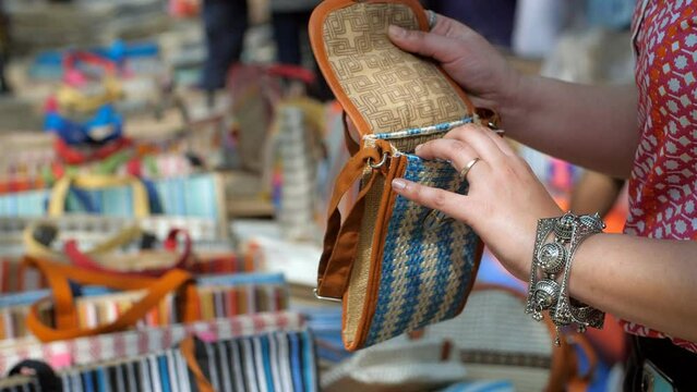 Close-up of Indian woman shopping for handmade jute wallet - shop in  handloom market. A woman checking a new sling bag from a local Indian market or fair/mela - An artisan market with hand-made pr...