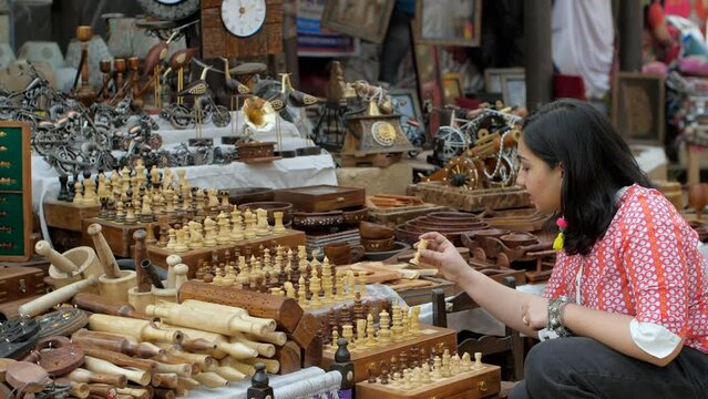 A beautiful Indian woman choosing wooden chess set in the bustling Indian market - Indian fair  Surajkund mela  traditional wooden crafts. A woman doing shoppoing in a street market in India - ches...