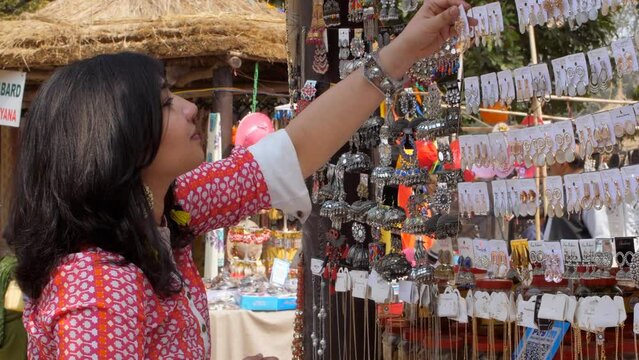 Asian woman looking for fancy jewelry and accessories in a flea market shop - Street shopping . A beautiful lady choosing earrings from a street vendor in the market - earrings shopping  handcrafte...