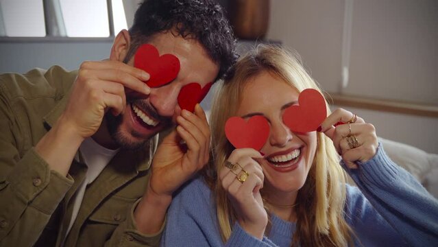  Close-up photo of happy couple in love hiding eyes behind paper hearts.