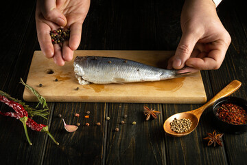 The cook prepares mackerel fish on a kitchen cutting board. Adding dry pepper to fish herring