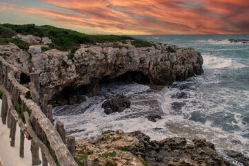 Sea waves crashing against the rocks next to buildings.