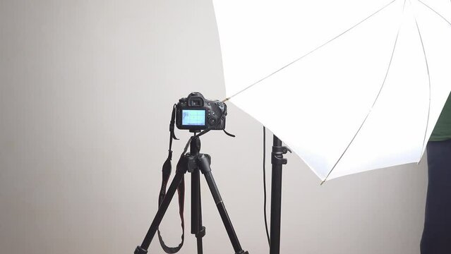 Photo camera on tripod and studio umbrella light adjustment for shooting