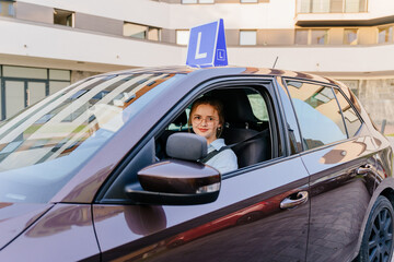 Portrait of a happy woman confident in her skills driving car with blue L plate on a roof at the lesson of driving school. Driving school and people concept.