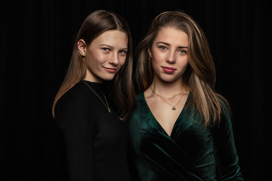 Studio shot of two young sisters arm in arm elegantly dressed with positive attitude
