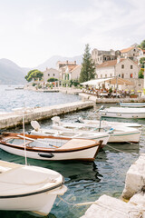 Fototapeta na wymiar Row of fishing boats moored at the Perast pier against the backdrop of ancient stone houses at the foot of the mountains. Montenegro