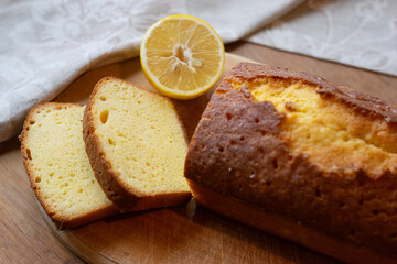 Homemade sliced pound cake with half of lemon on a cutting board on a wooden background.