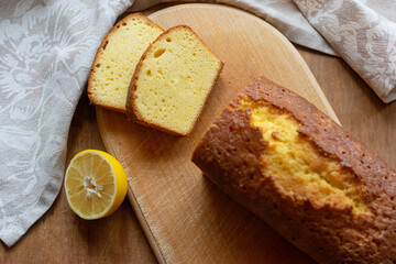 Homemade sliced pound cake with half of lemon on a cutting board on a wooden background.