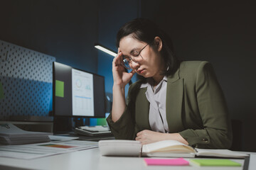 Young Asian businesswoman working overtime in a dark office, Young woman working on the laptop late at night, working overtime in the office to finish the project within the deadline.