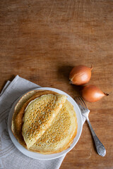 Crepes (Russian Blini) with onions on wooden background, top view, copy space. Homemade thin fresh crepes for breakfast