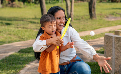 A boy with Down syndrome learns from his mother how to play tennis in a natural park.
