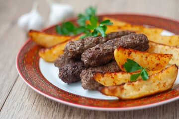 Lula kebabs on a white plate with a red border with baked potatoes and greens.