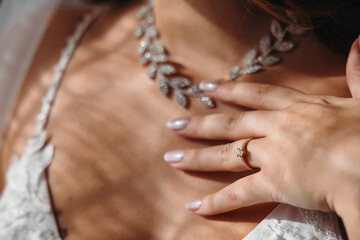 Charming beautiful bride in her wedding dress is elegantly touching her necklace. Light comes through the curtain window