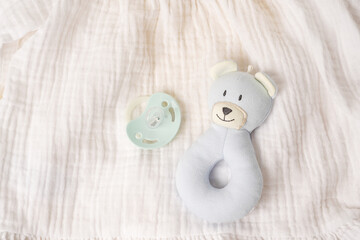Blue toy bear and baby pacifier on white textile background