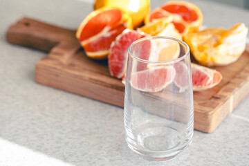 Empty glass and fresh sliced oranges on wooden board in the kitchen.